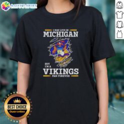Official ladies tee featuring 'I May Live In Michigan But I'm A Minnesota Vikings Fan Forever' design.