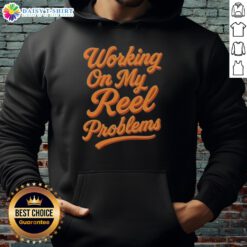 Person wearing an Awesome Working On My Reel Problems Fishing Hoodie while fishing by the lake, enjoying outdoor life.